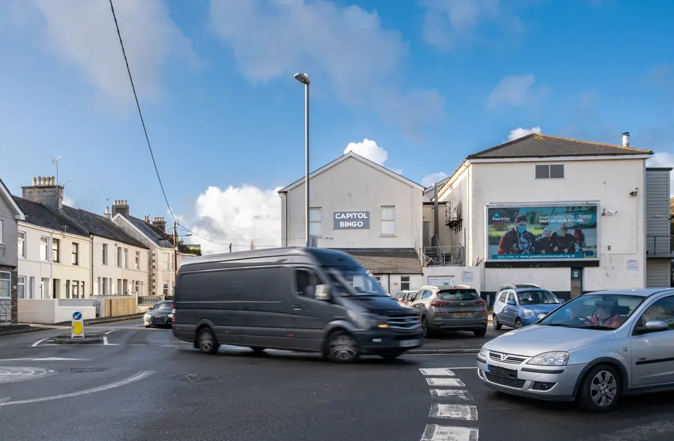 A van passing the Alexandra Road junction in St Austell, billboard on the building behind