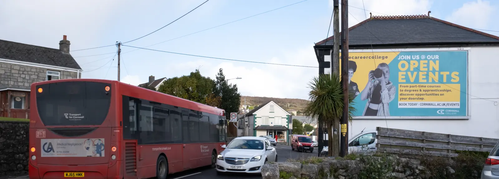 A red bus passing the Tregonissey Road billboard in St Austell
